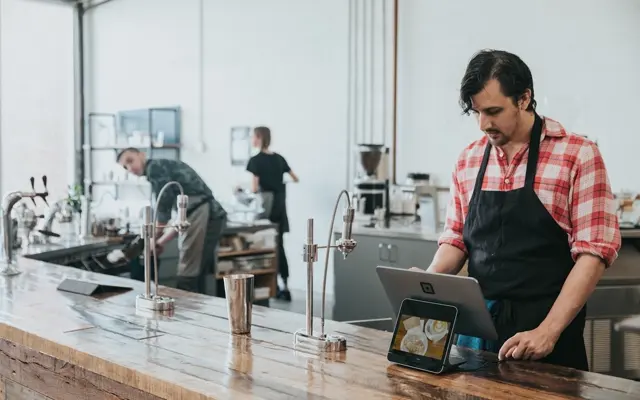 A cafe owner in an apron working at the counter of his shop
