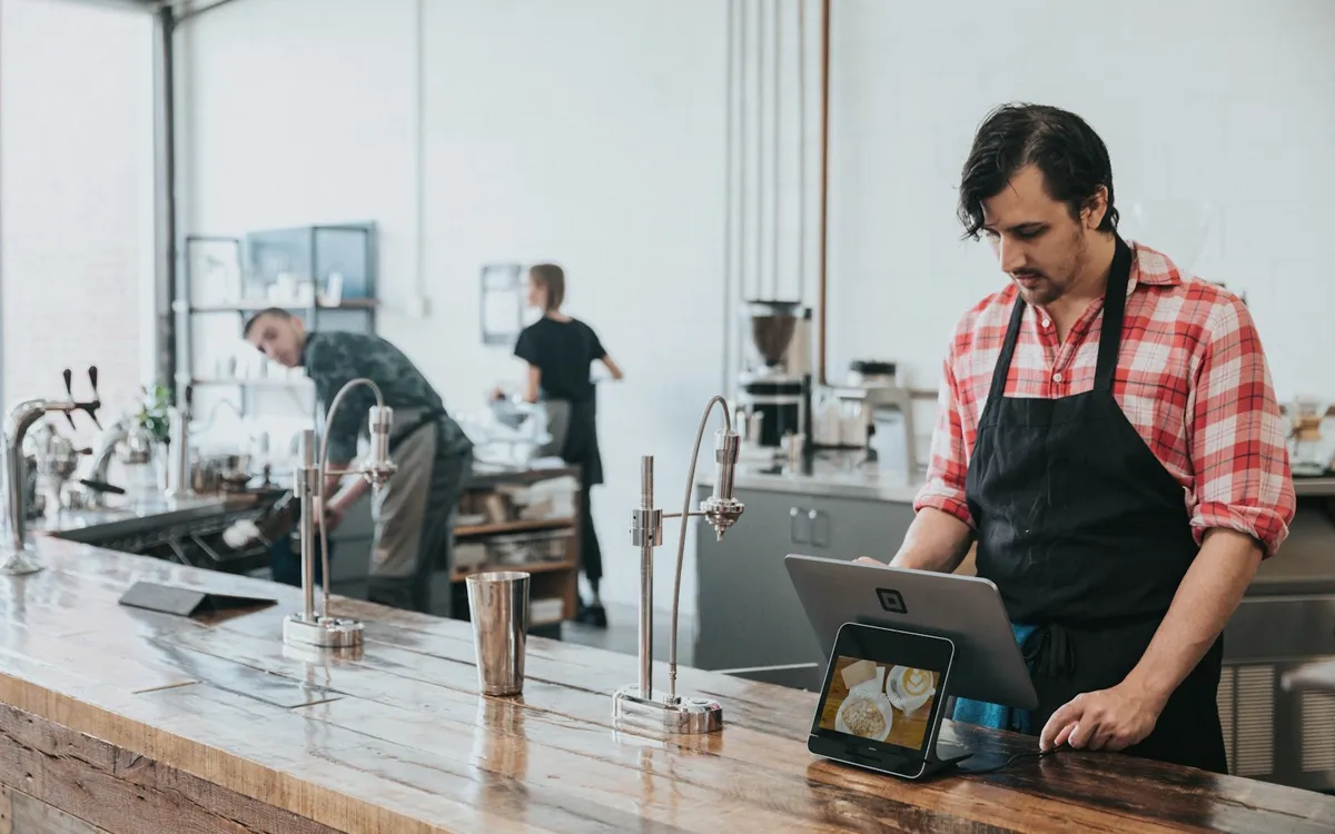 A cafe owner in an apron working at the counter of his shop