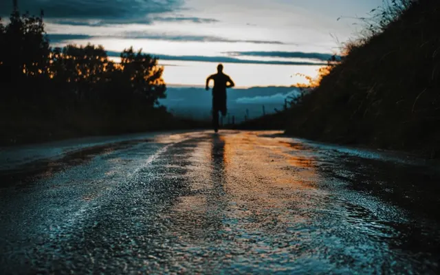 A runner on an empty wet road at dusk