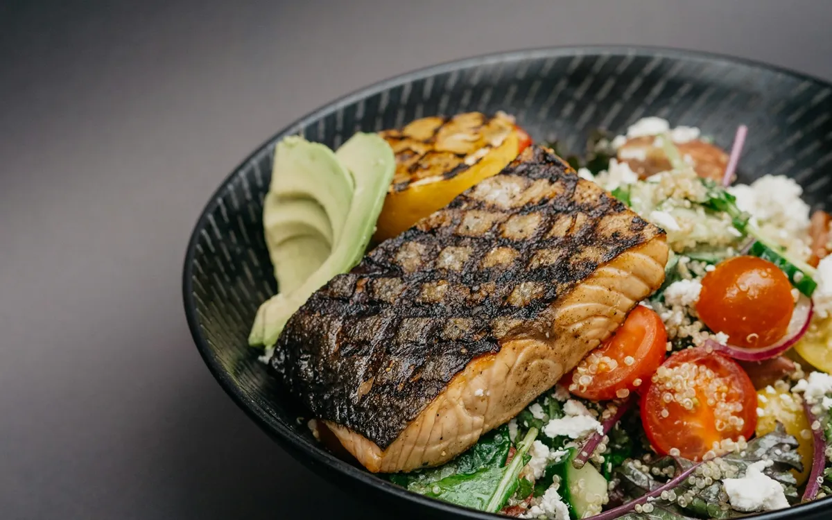 Grilled salmon with avocado, tomatoes and greens in a dark bowl