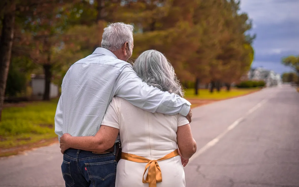An older couple walking arm in arm down a tree-lined road