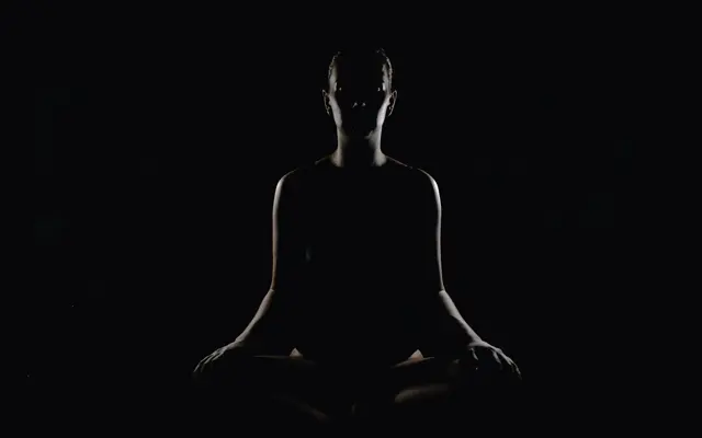 The silhouette of a person meditating in a dark room