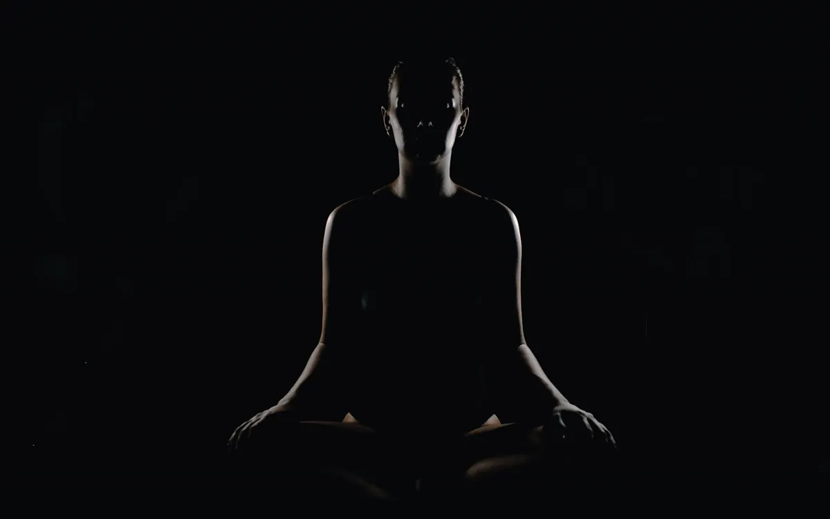 The silhouette of a person meditating in a dark room