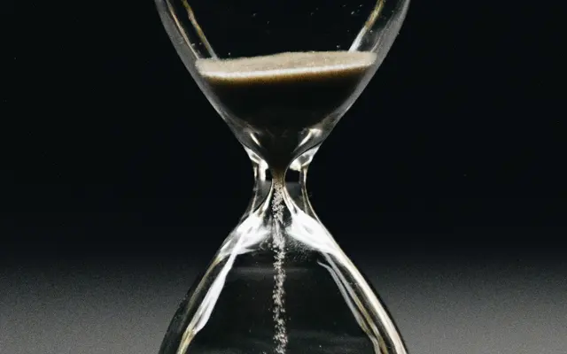 Sand running through an hourglass against a dark background