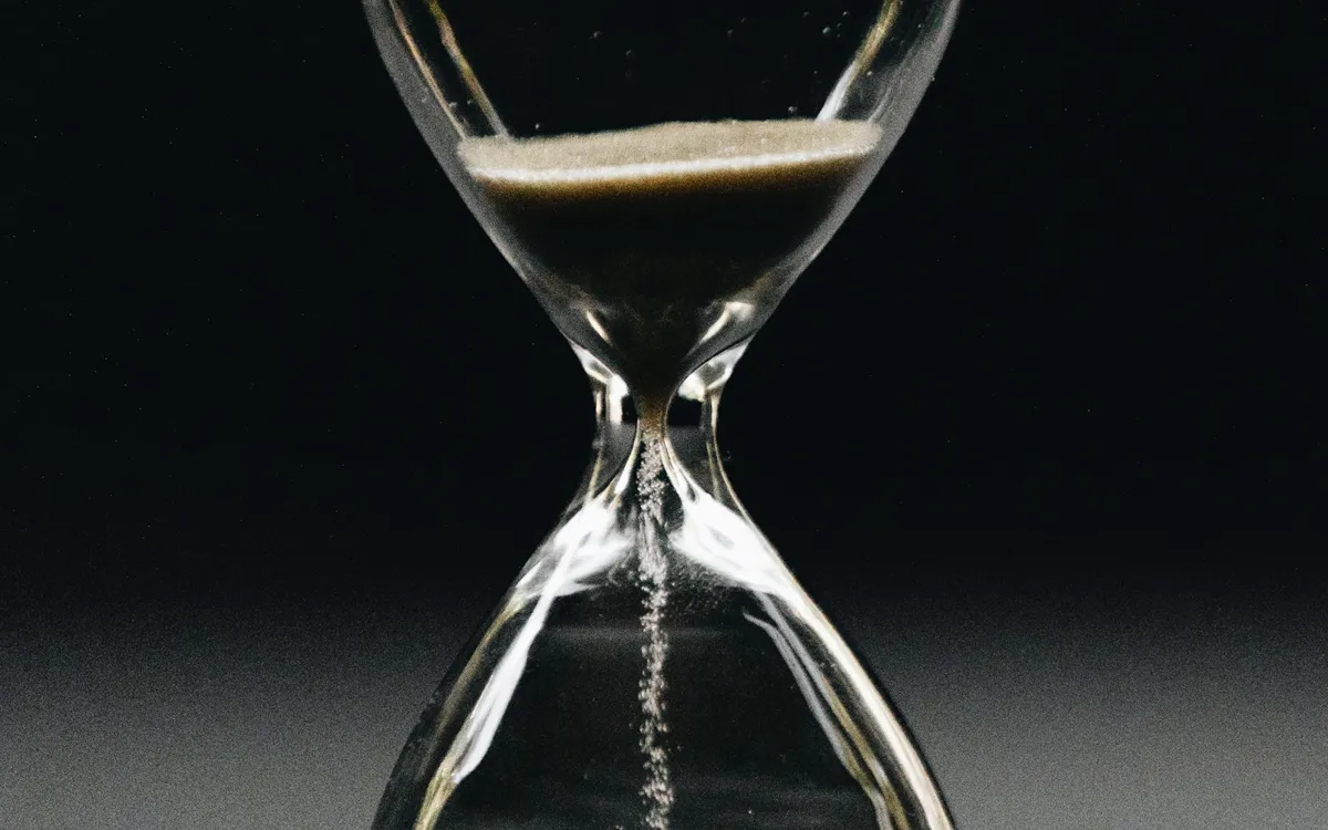 Sand running through an hourglass against a dark background
