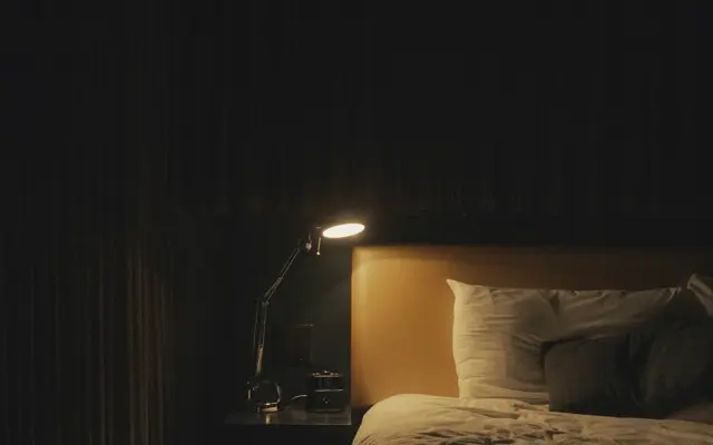 A dim bedroom lit by a single bedside lamp