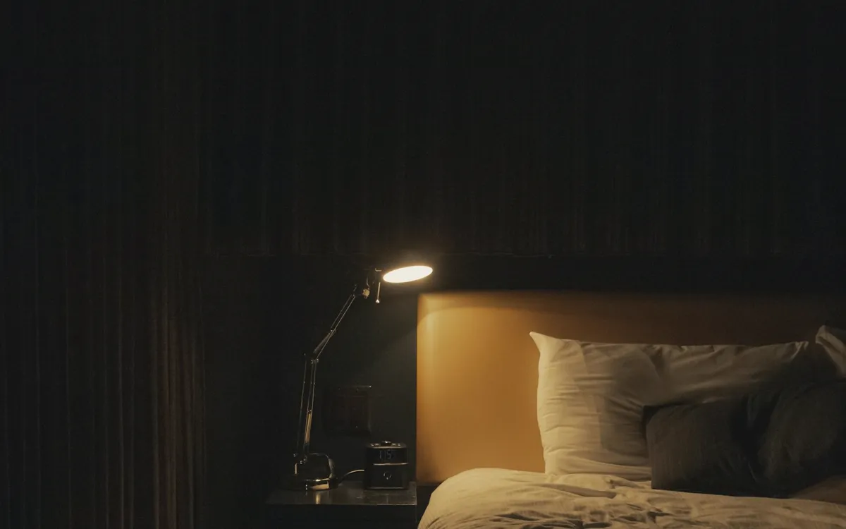 A dim bedroom lit by a single bedside lamp