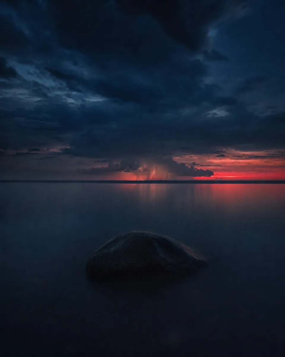 A still, dark sea with one stone rising from the water